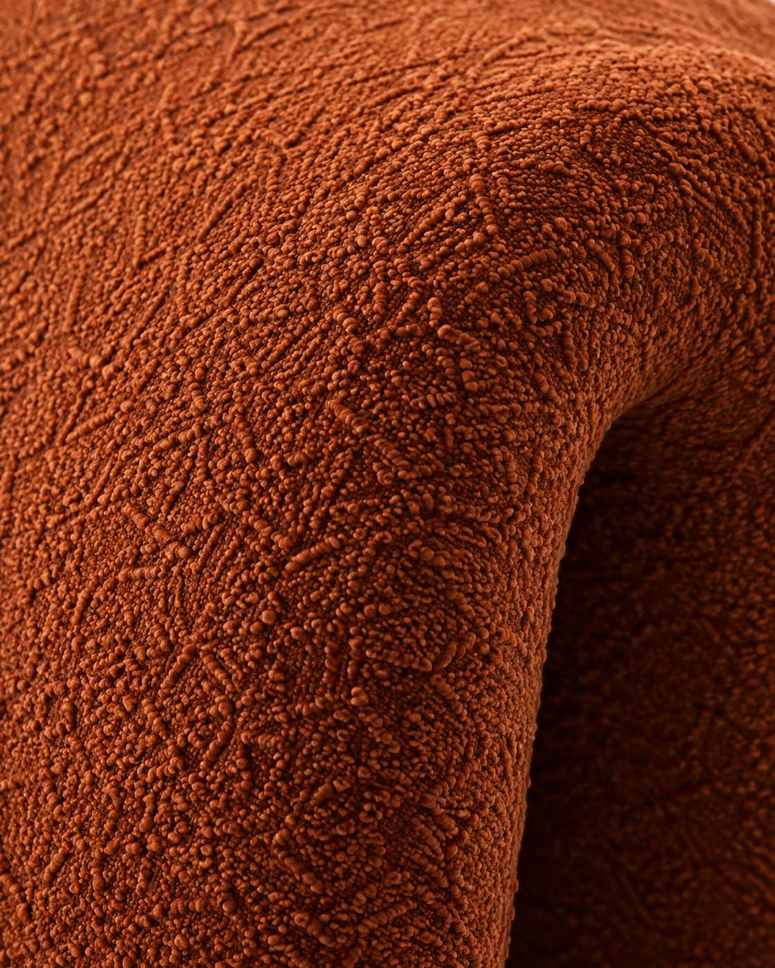 Close-up of the rust bouclé upholstery, its looped texture catching the light